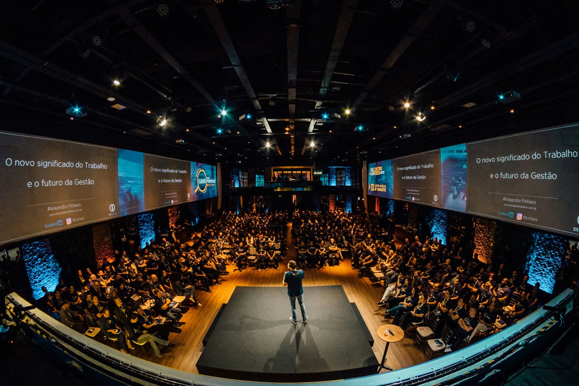 A speaker addresses a packed conference auditorium from centre stage