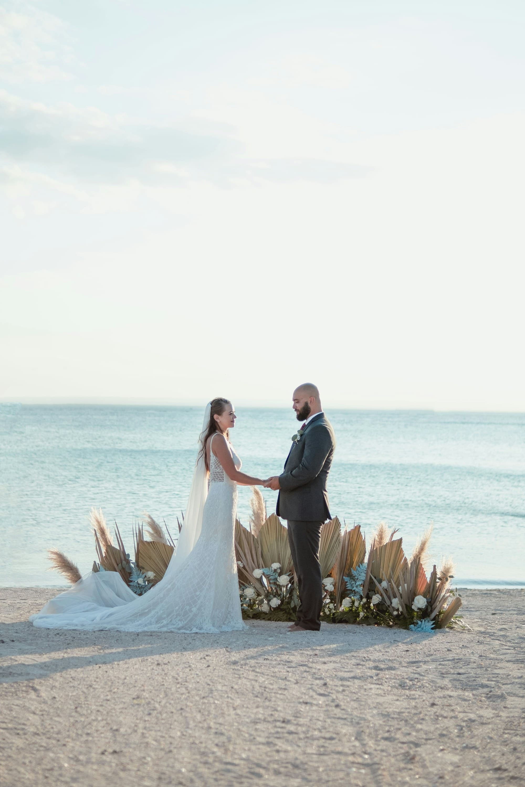 A bride and groom hold hands while standing on a beach