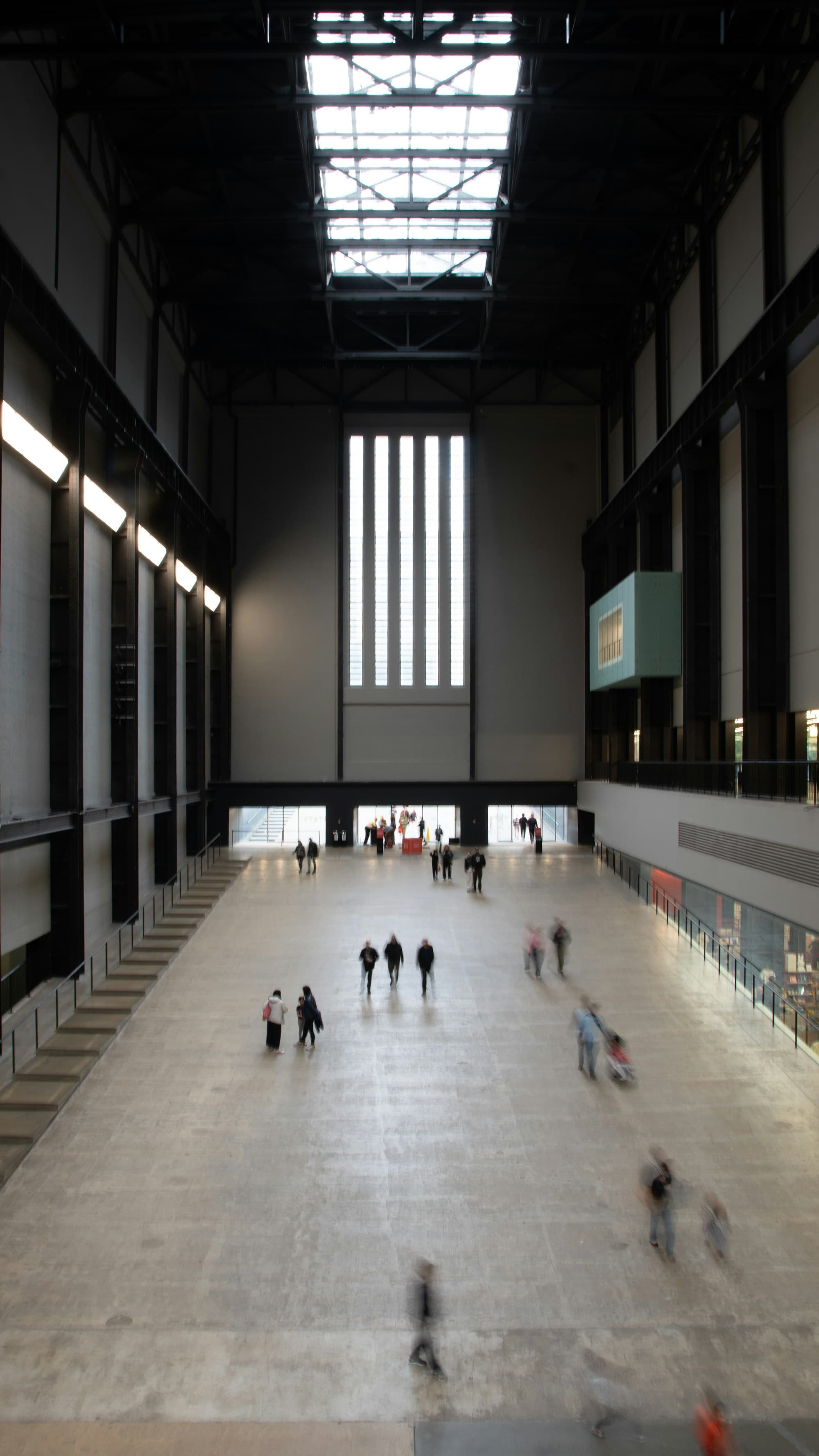 A vast industrial exhibition hall with soaring skylights and small figures below