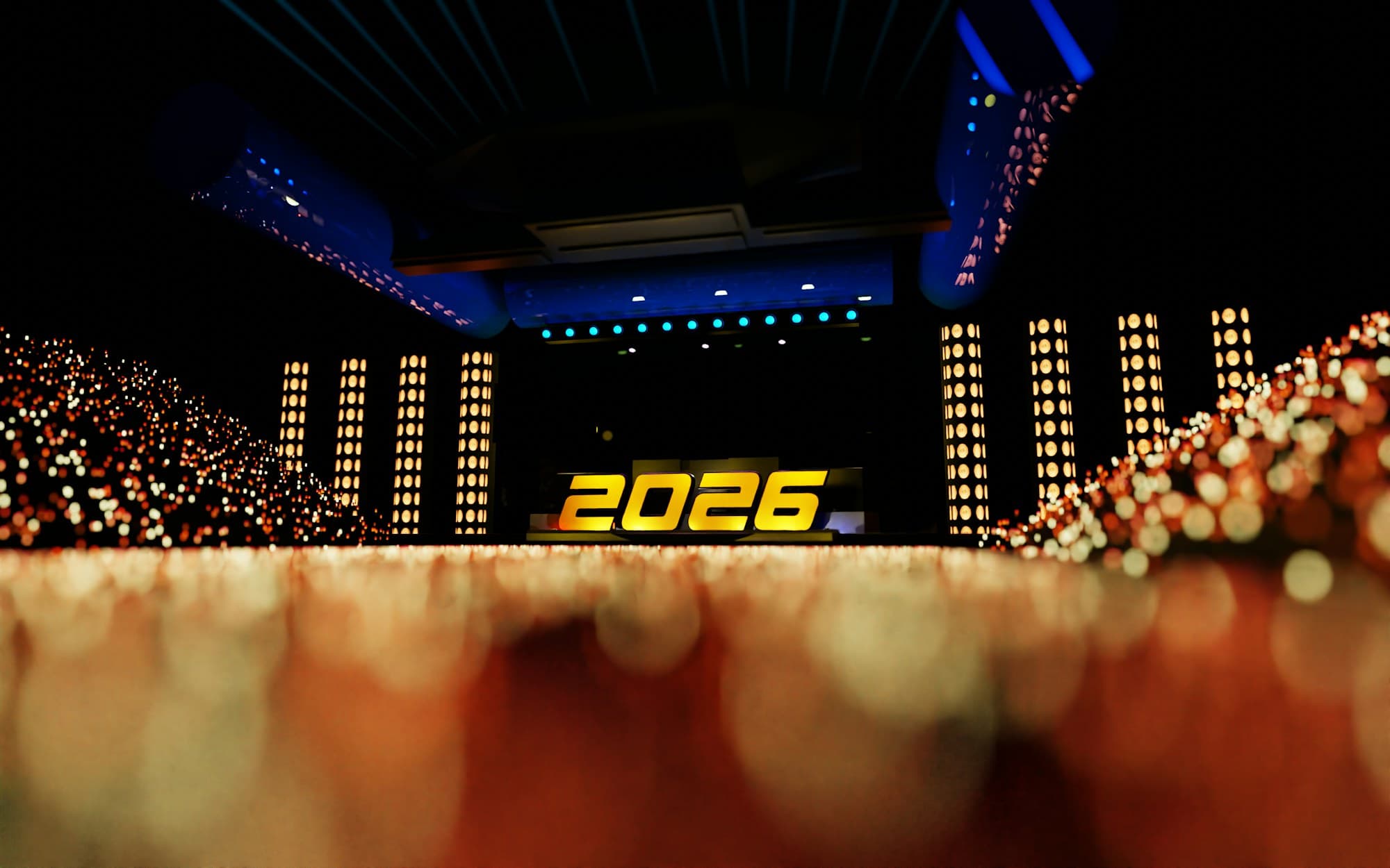 A grand celebration stage lit with golden light pillars and laser beams above a crowd