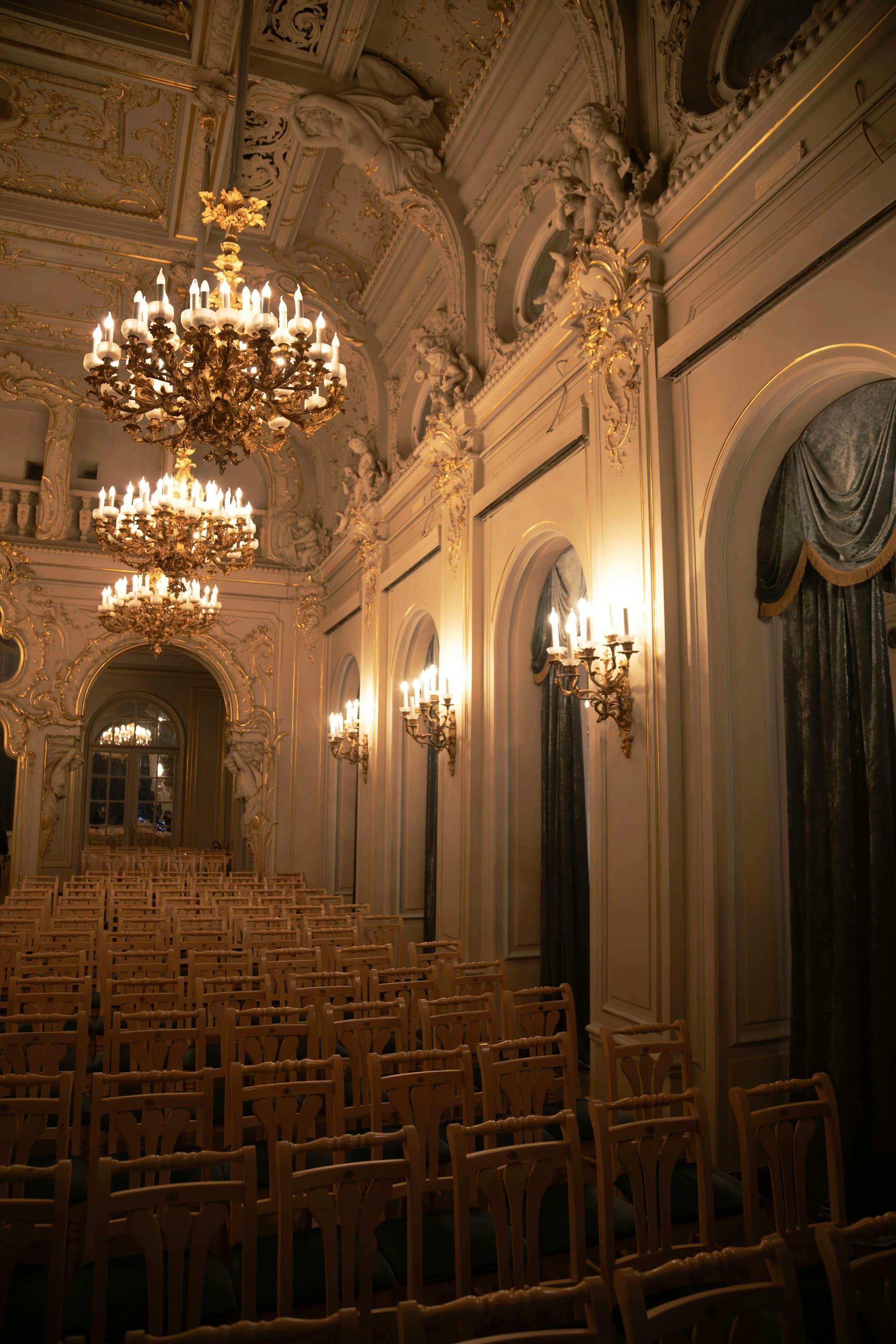 An ornate ballroom set with rows of chairs beneath grand chandeliers