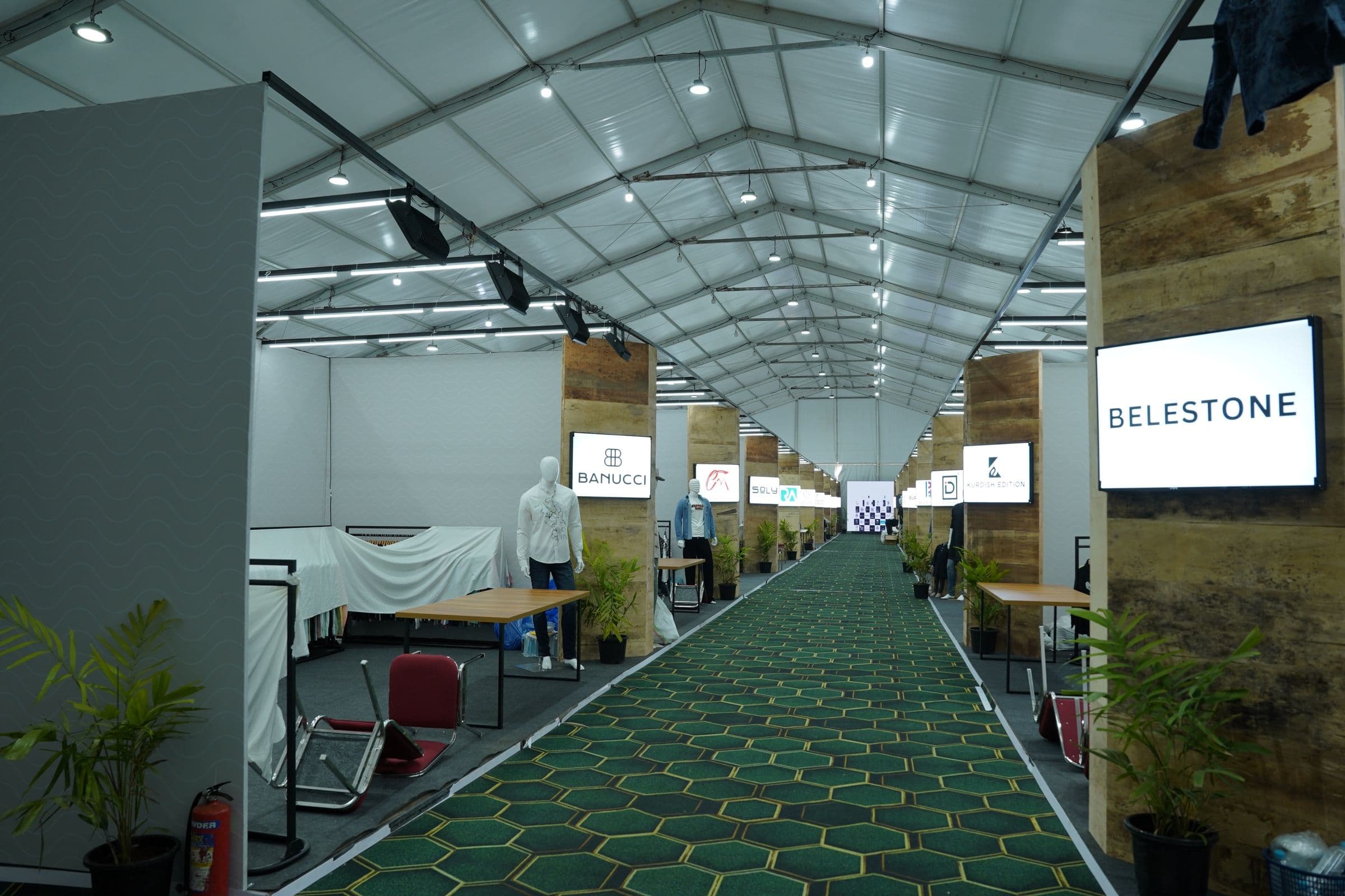 A green-carpeted exhibition aisle between white shell-scheme stalls