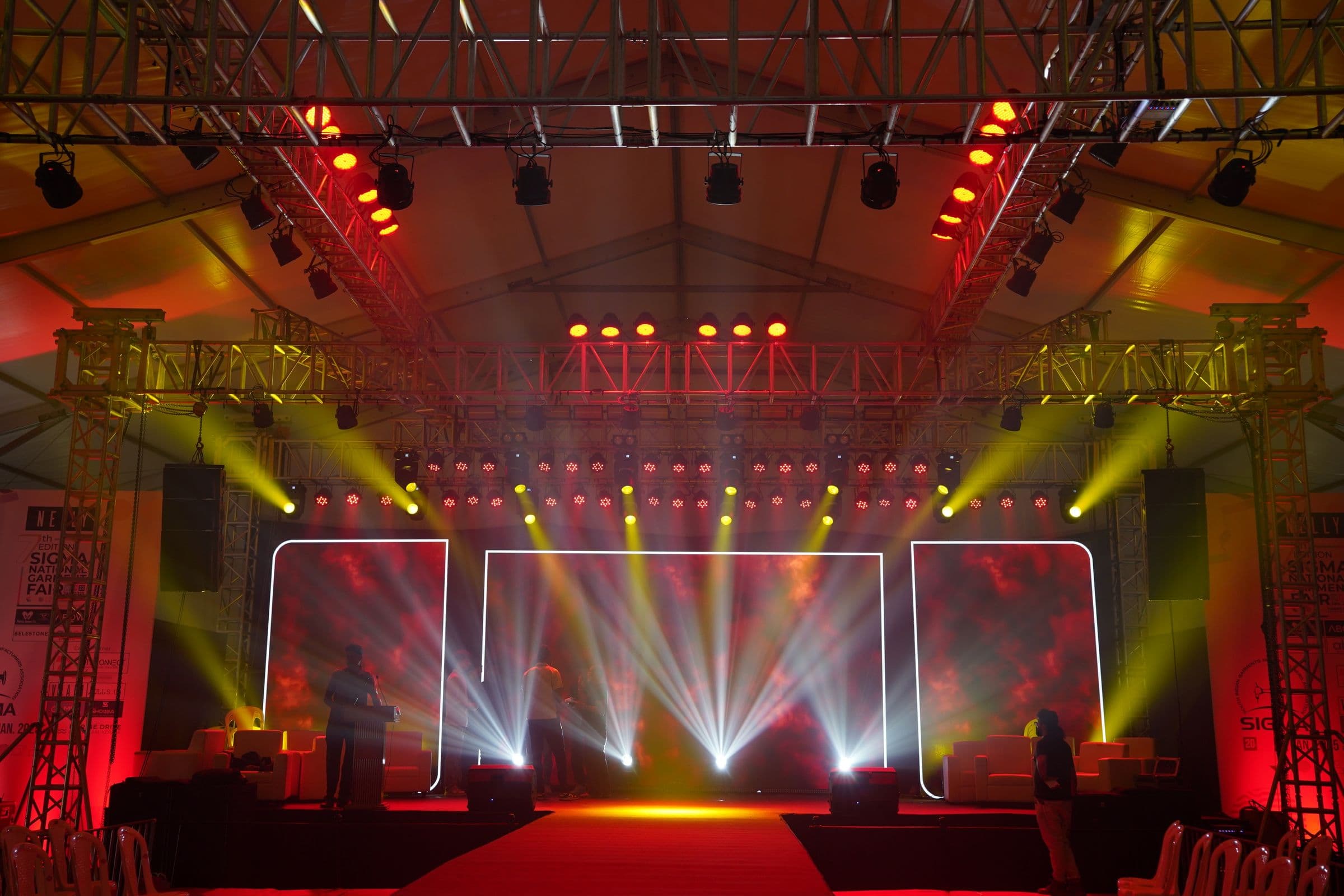 Stage lighting fires across a performance set under a tented hall