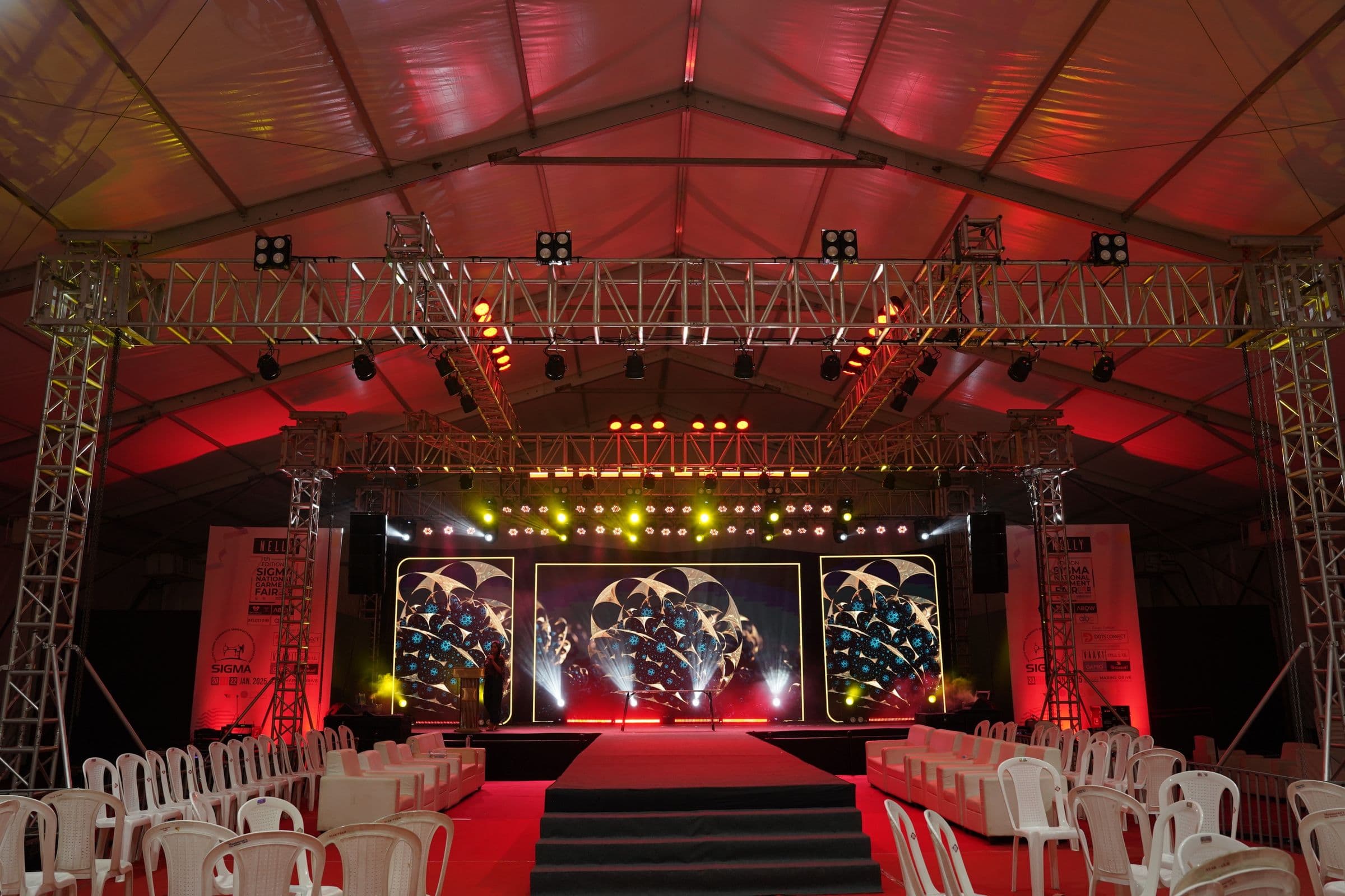 A red-lit stage and seating built inside a temporary event structure