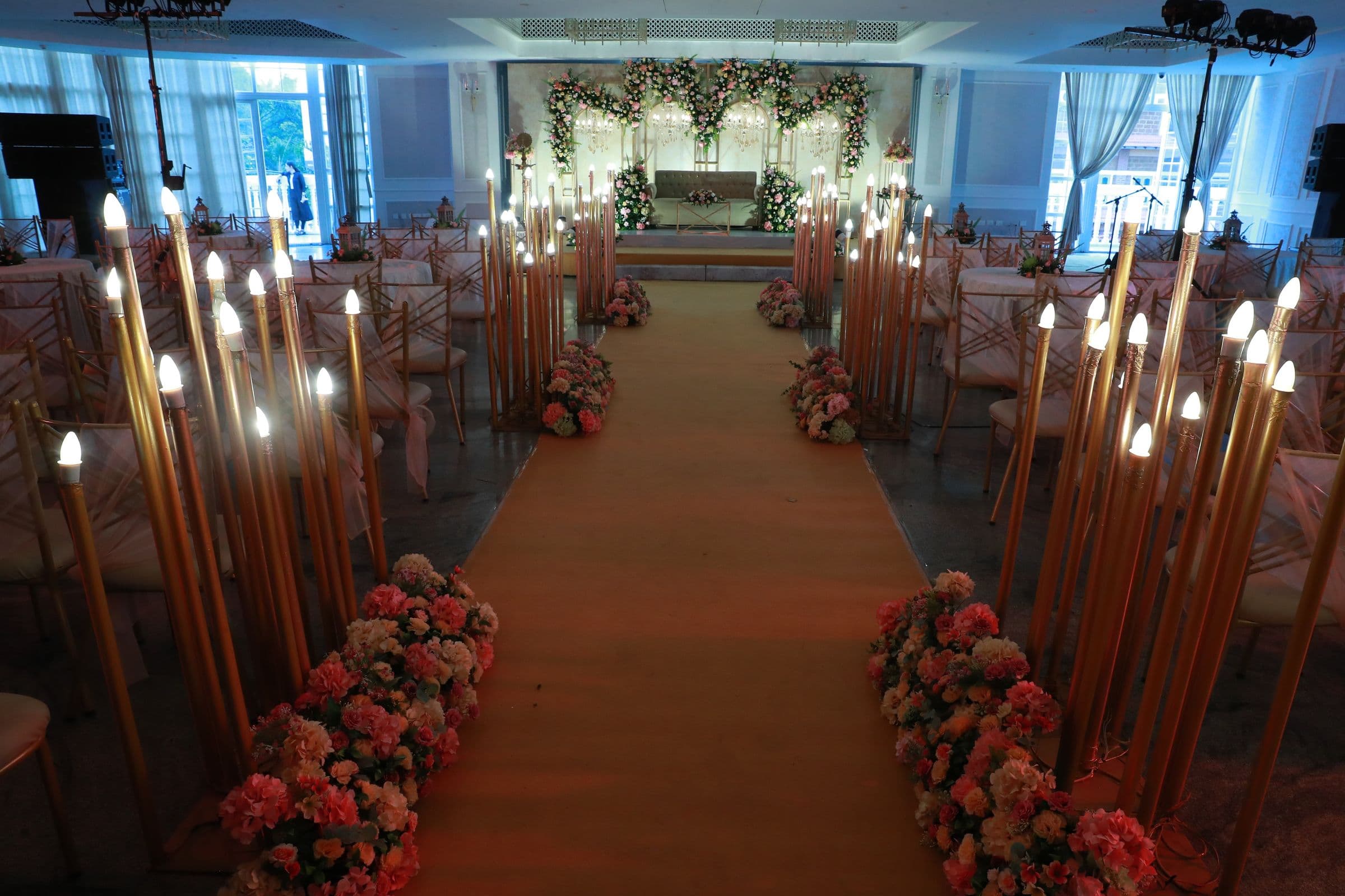 A wedding aisle lined with tall candles and roses leading to the stage