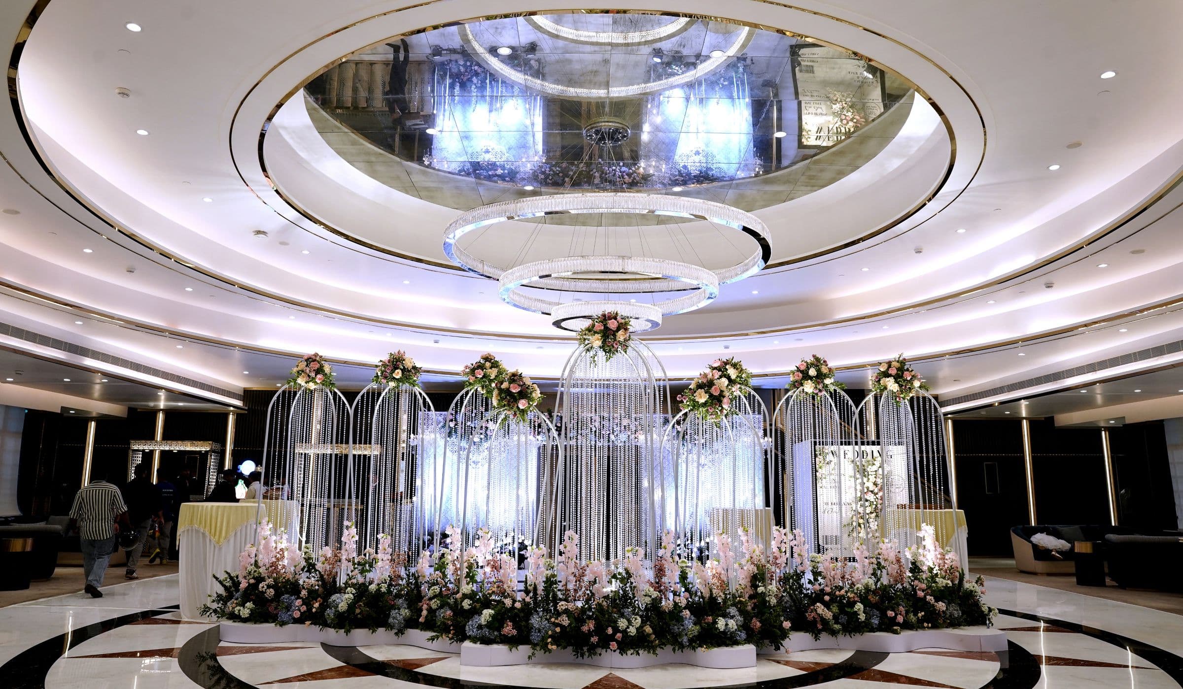 A domed wedding reception hall with a floral stage beneath a crystal chandelier