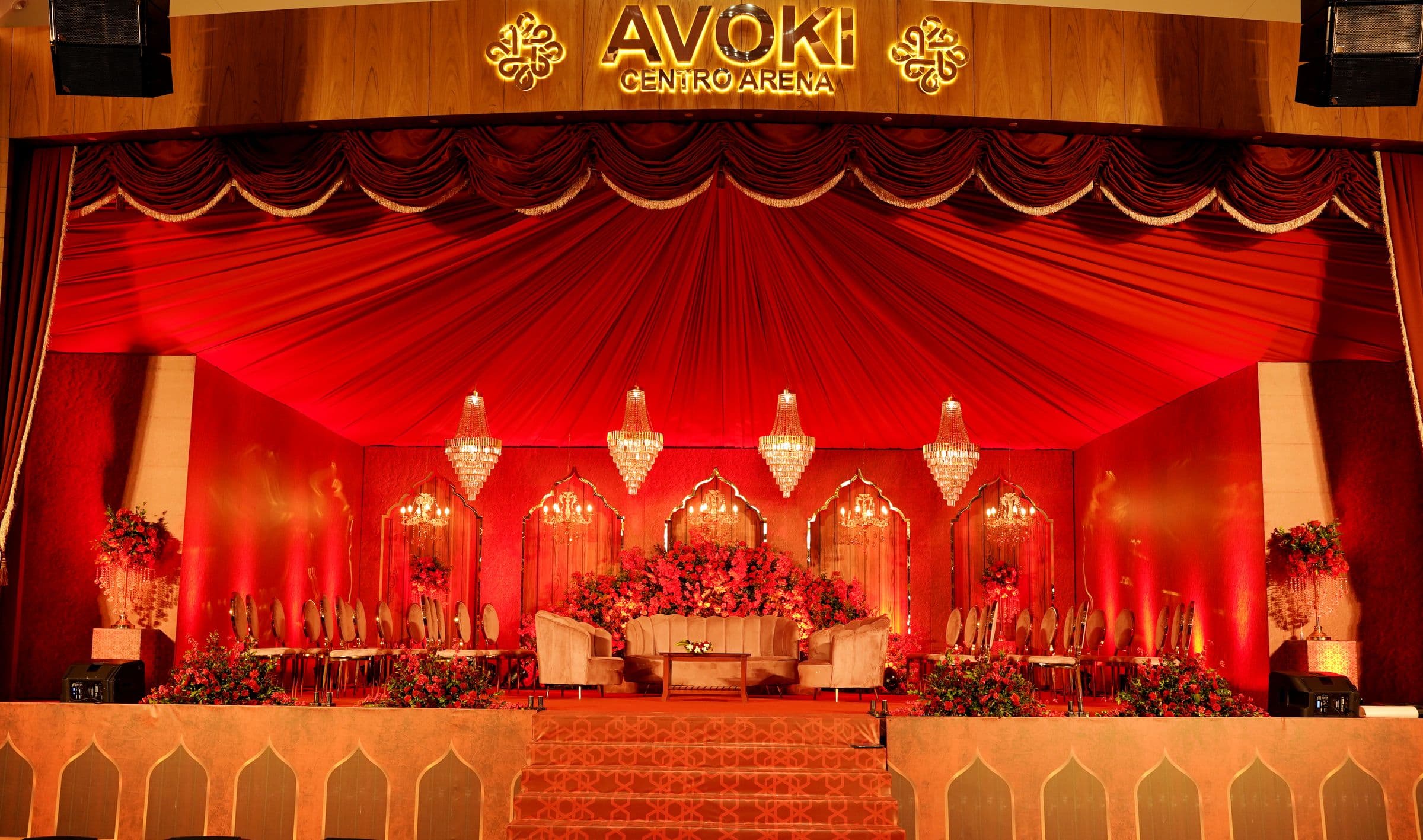 A red and gold wedding stage with draped backdrop and chandeliers