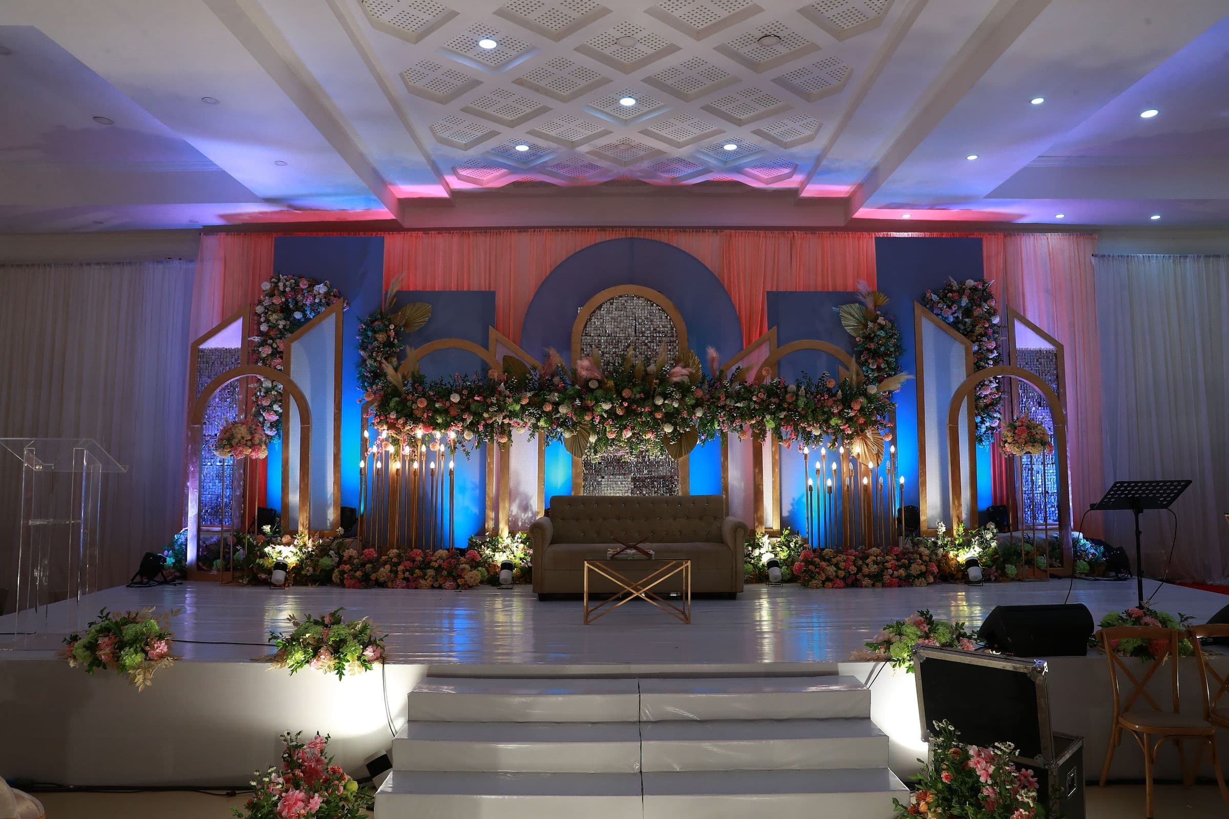 A wedding stage lit in blue and pink with floral arches