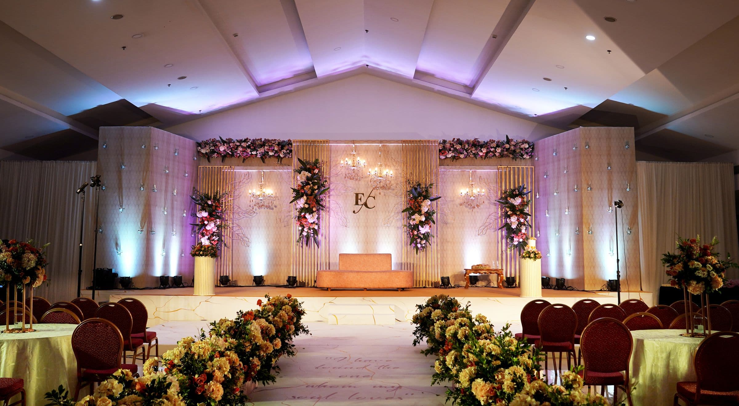 A pastel wedding stage framed by floral arrangements and warm uplighting