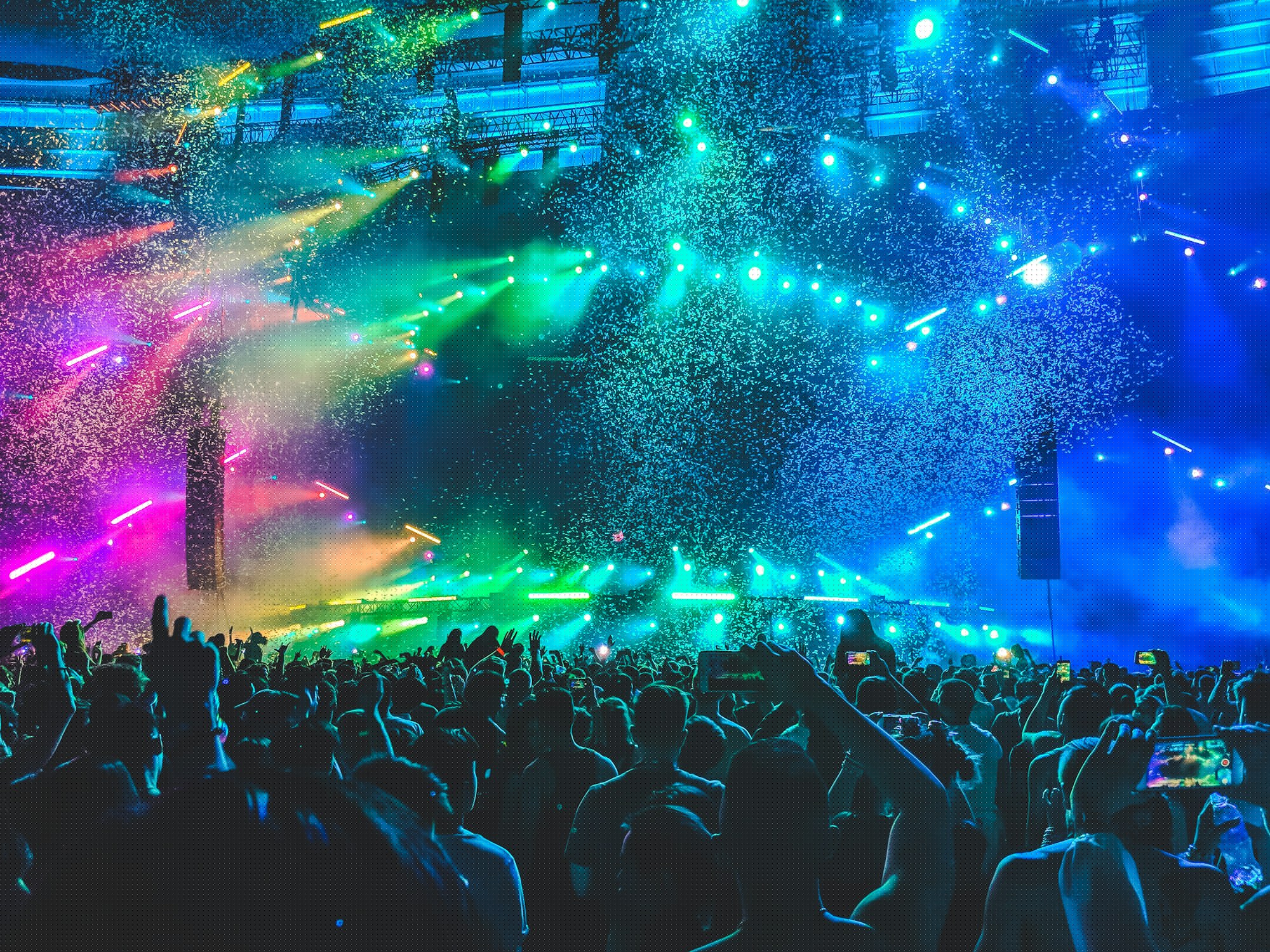 A packed festival crowd faces a brightly lit main stage at night