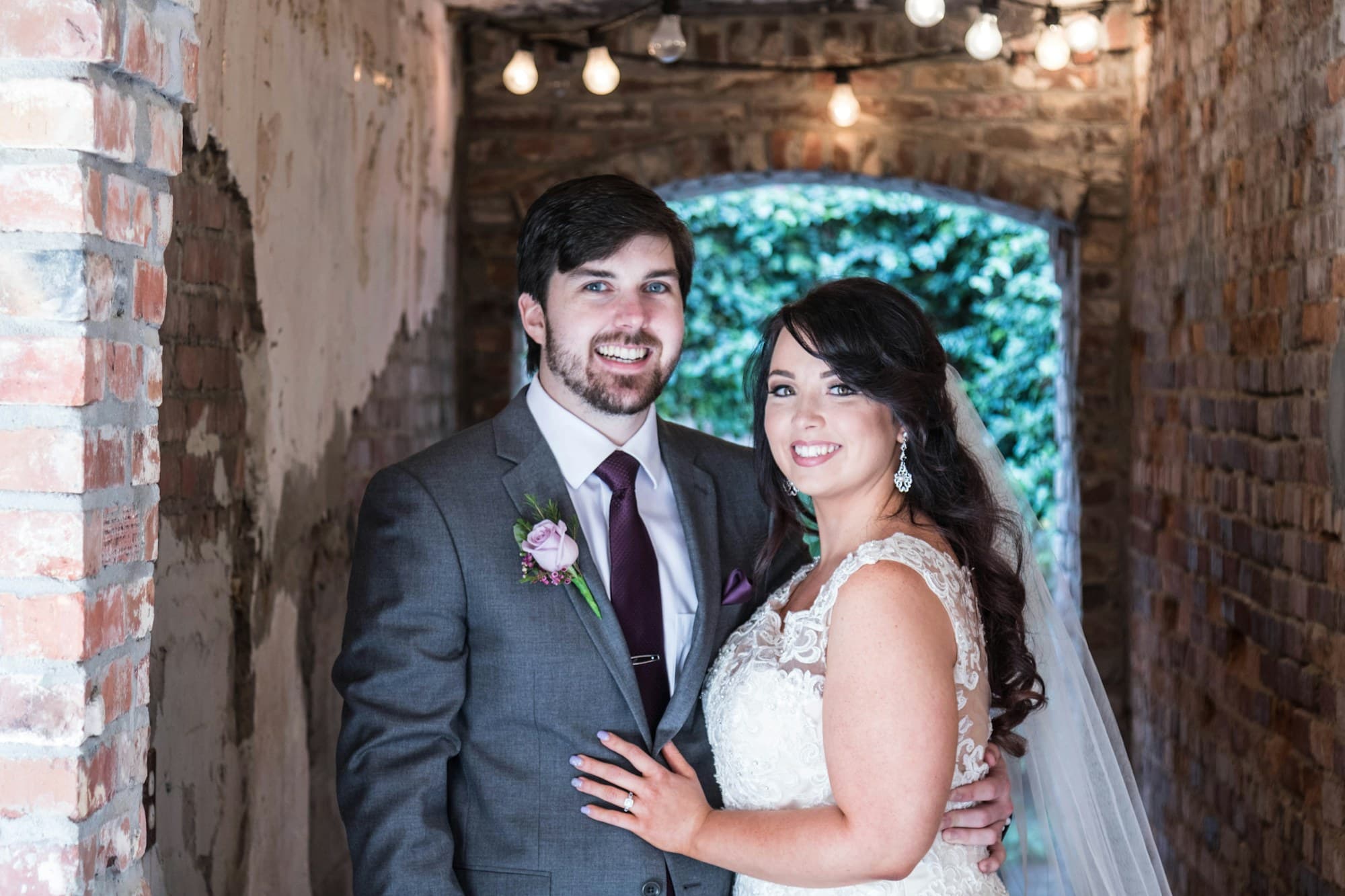 A groom in a black suit stands beside his bride in a white wedding gown